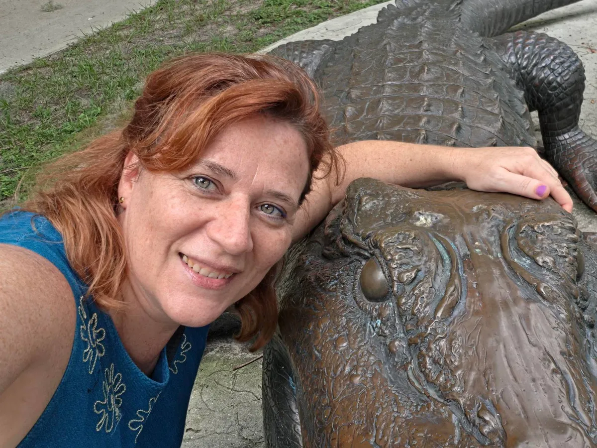 Nadia smiling with her arm resting on a bronze alligator statue